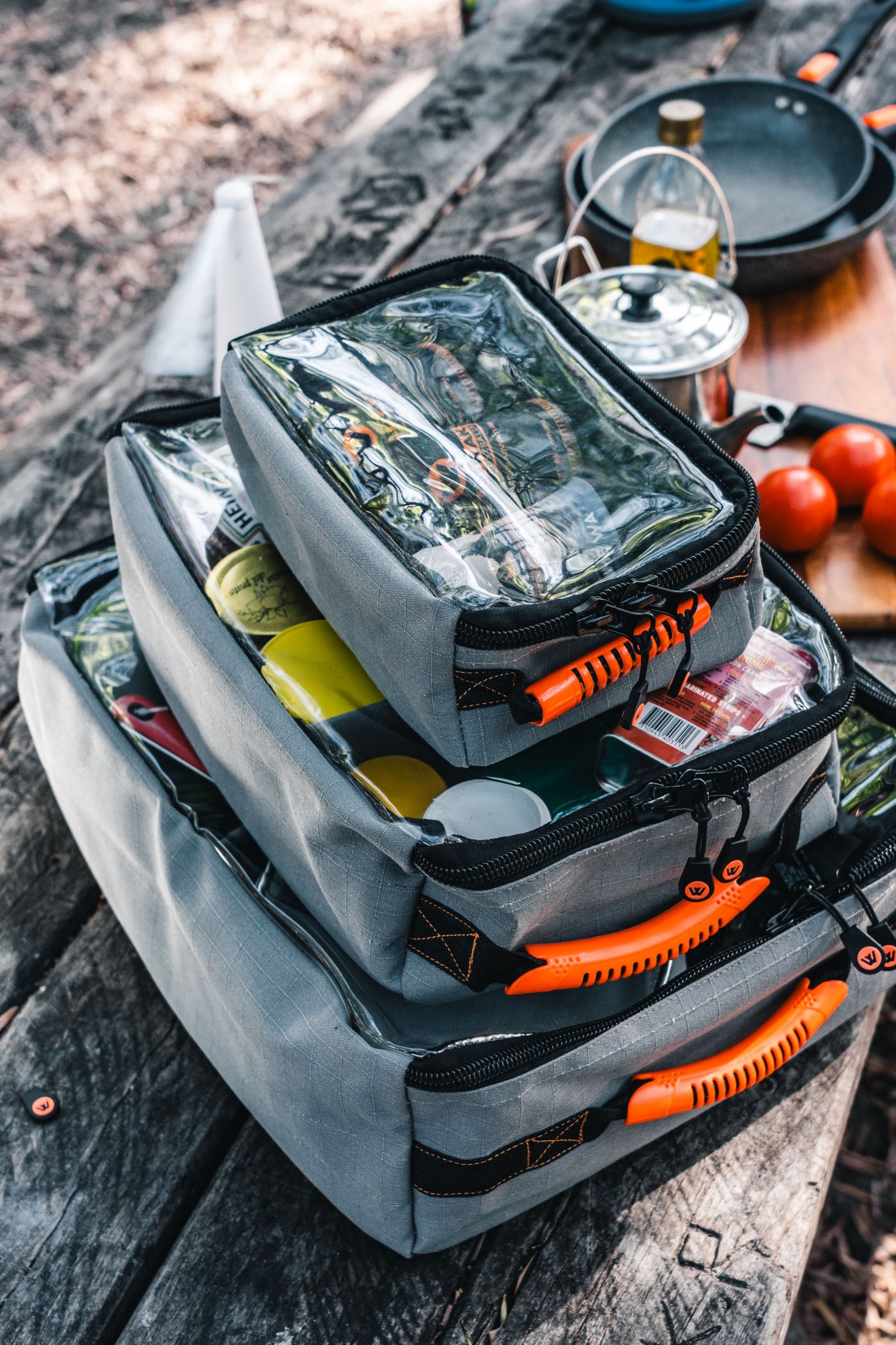 Stacked Wildtrak canvas bags for camping on a picnic table with outdoor cooking gear.