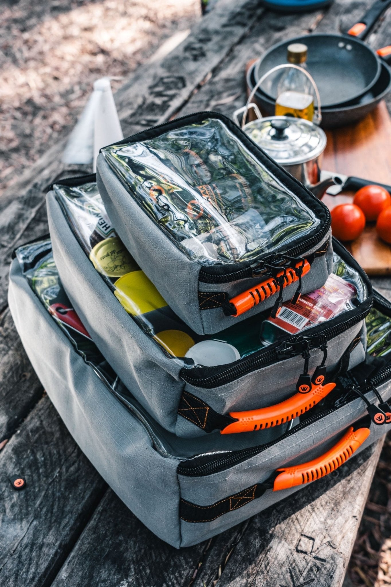 Stacked Wildtrak canvas bags for camping on a picnic table with outdoor cooking gear.